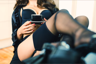 Eine Frau in schwarzen Dessous sitzt mit Kaffee auf einem Stuhl.
