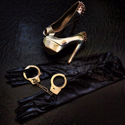 Lederhandschuhe, Handschellen und High Heels auf schwarzem Untergrund.