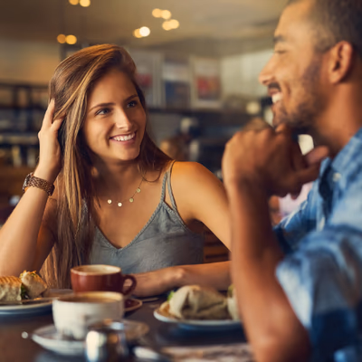 Eine Frau und ein Mann sitzen bei einem Date zusammen. Die Frau lächelt interessiert.